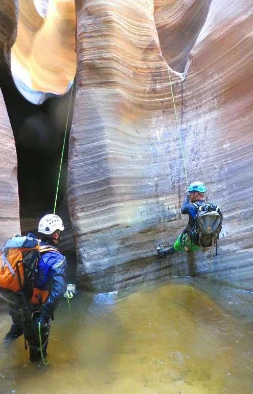 Helmeted canyoneers beside bands of sculpted sandstone