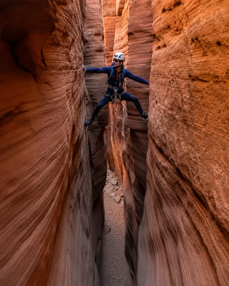 A helmeted canyoneer stemming between sandstone walls